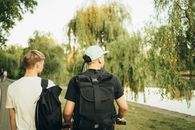 两个年轻人背着背包，走在阳光明媚、绿树成荫的公园里