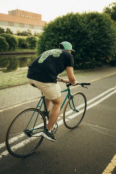 一名男子骑着自行车，穿行在城市道路上，背景是绿化和建筑