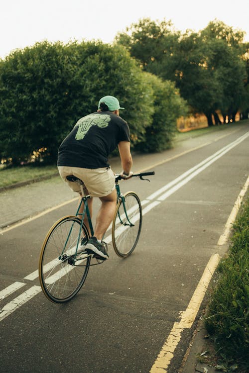 Man in Black T-shirt Riding Bicycle on a Bike Lane