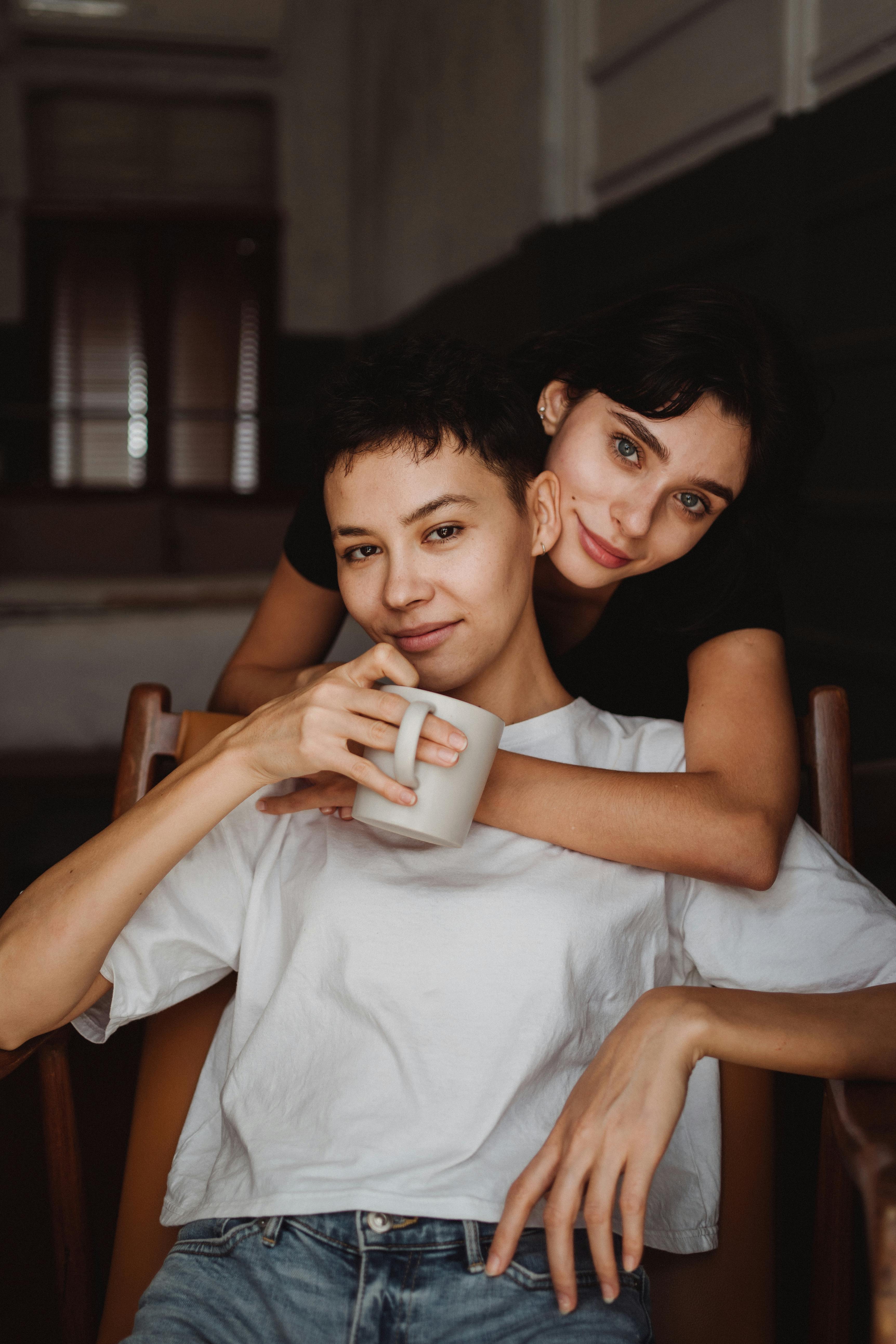 woman hugging girlfriend drinking coffee from behind