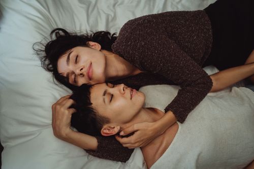 Free A loving couple enjoys a tender moment, lying together with eyes closed in a cozy setting. Stock Photo