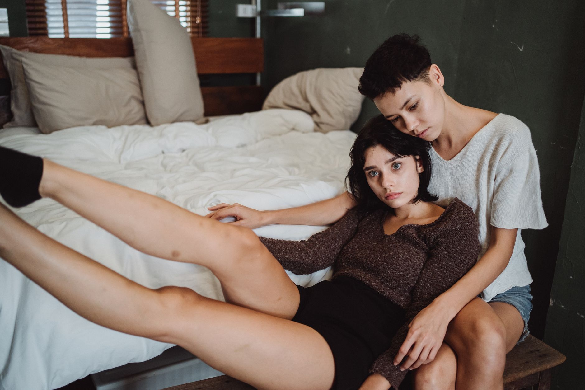Two women share a quiet intimate moment together in a bedroom, embracing each other.