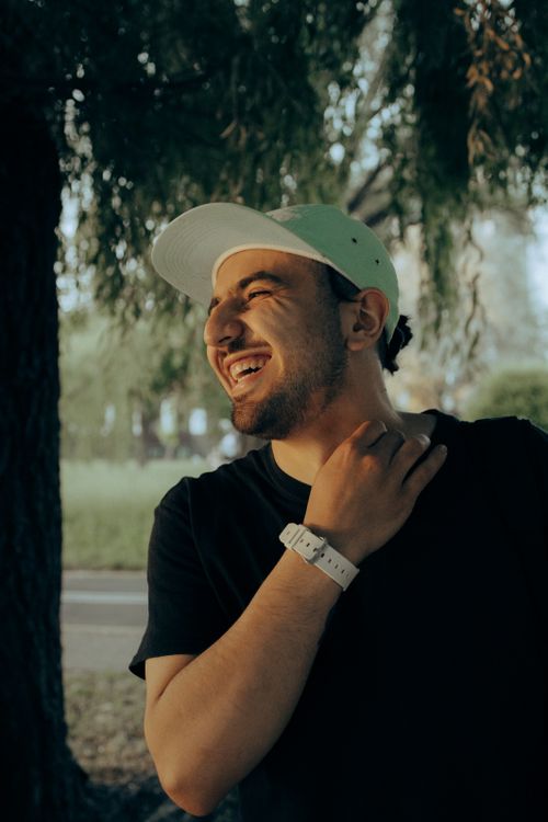 Free A joyful young man laughs outdoors on a summer evening, wearing a white cap and watch. Stock Photo