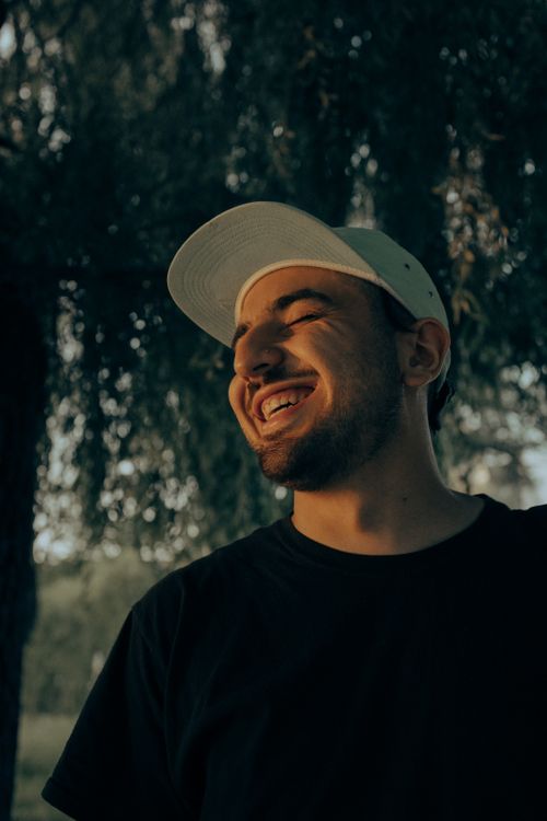 Free Close-up of a young man smiling with eyes closed, wearing a cap outdoors. Stock Photo