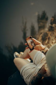 A person in casual shorts enjoying a tranquil moment by a lakeside, browsing a smartphone.
