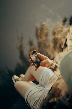 A young adult relaxing outdoors, browsing a smartphone while enjoying the natural surroundings.