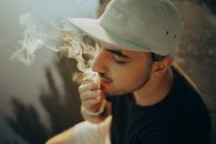 一个年轻人戴着帽子抽烟的特写镜头，周围烟雾缭绕
