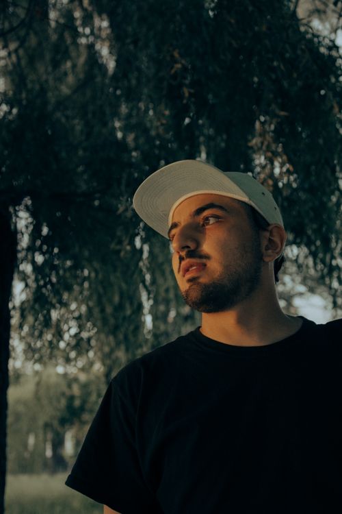 Free Man in a black shirt and cap looking away, captured outdoors with moody lighting. Stock Photo