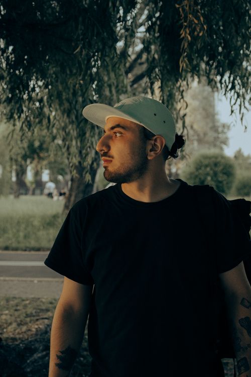 Free Portrait of a man in a cap looking sideways, captured in a tranquil outdoor setting with tree background. Stock Photo