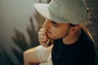 一个戴着帽子的年轻人坐在湖边抽烟，黄昏的氛围映照出几分喜怒无常