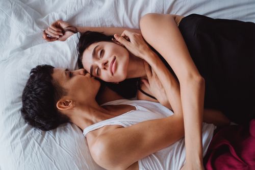 Free A loving same-sex couple sharing a tender embrace and kiss while lying in bed. Stock Photo