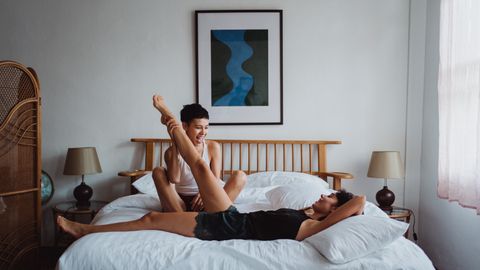 Two women having fun and laughing together in a cozy bedroom setting.