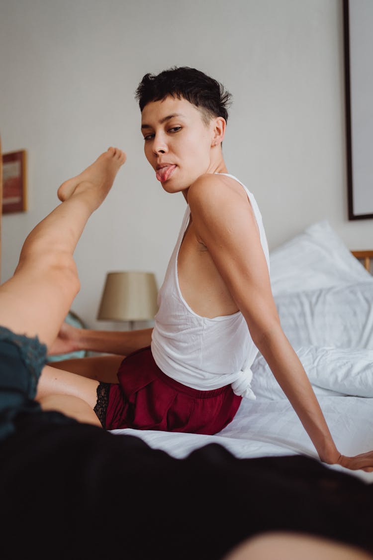 Woman Sitting On Bed Sticking Her Tongue Out