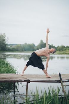 A man performing a yoga stretch on a wooden pier by a serene lake, perfect for wellness themes.