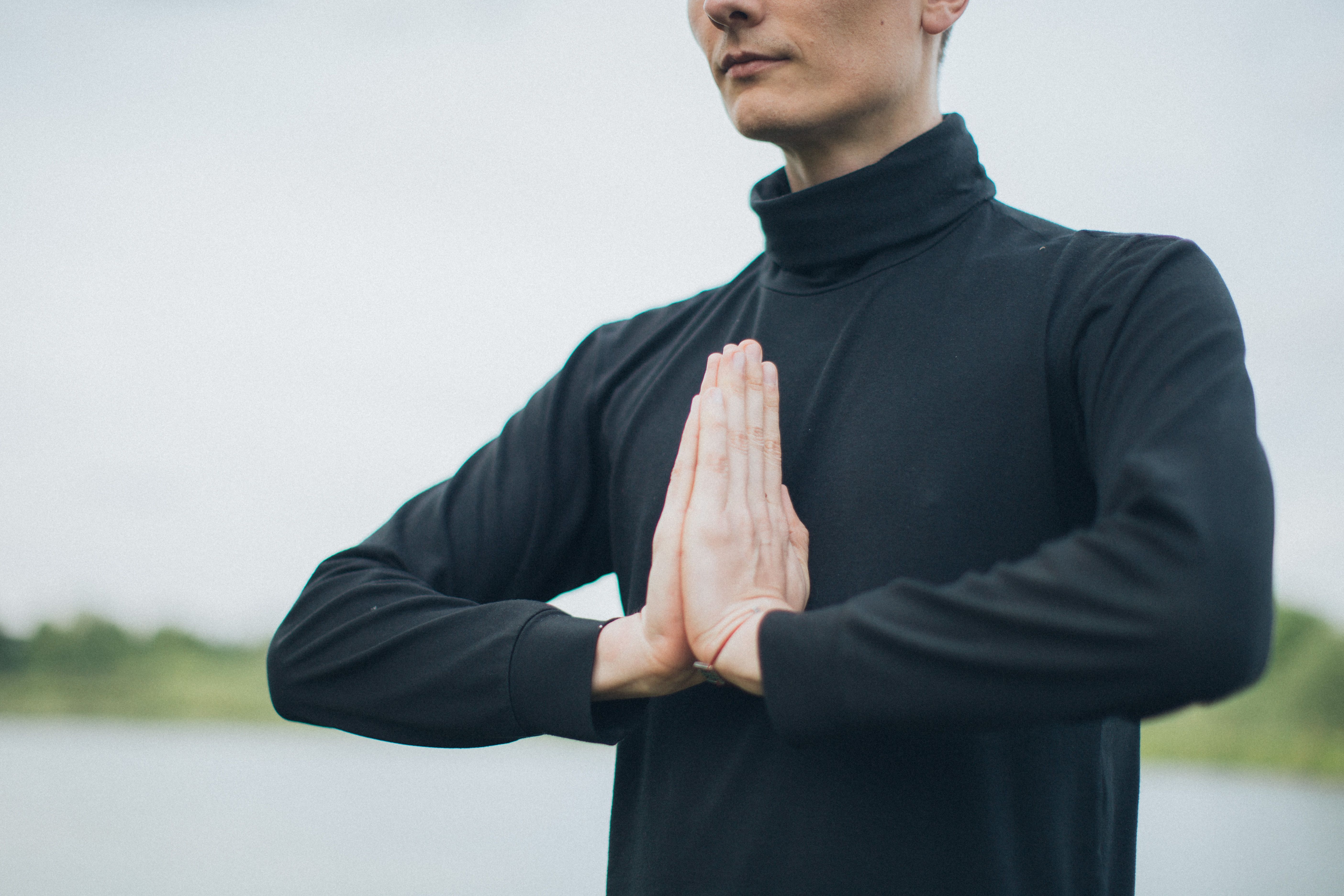 Close-up of a person meditating outdoors with hands in prayer position, promoting wellness.