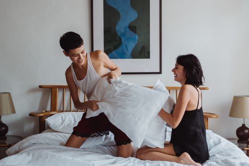 Free A cheerful couple having fun with a pillow fight in a cozy bedroom setting. Stock Photo
