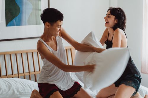 Free Two women having fun and enjoying a playful pillow fight in their bedroom, capturing moments of laughter and love. Stock Photo