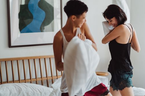 Free Joyful couple having a playful pillow fight in a cozy bedroom setting. Stock Photo