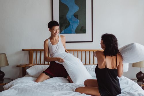 Free Happy couple playfully engaging in a pillow fight in a cozy bedroom setting. Stock Photo