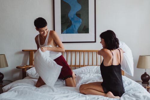 Free Two women having a playful pillow fight in a cozy bedroom setting. Stock Photo
