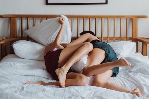 Free Two women engaged in a playful pillow fight on a bed, showing affection and love. Stock Photo