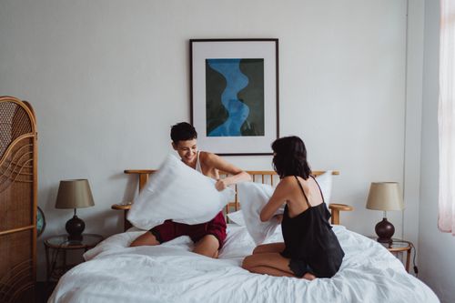 Free A happy couple enjoying a playful pillow fight in a modern bedroom setting. Stock Photo