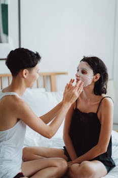 Two women sharing an intimate moment with skincare masks in a cozy bedroom setting.