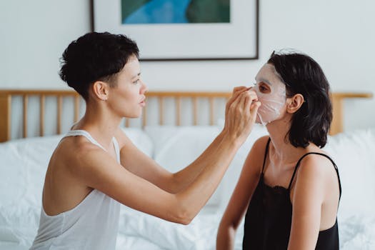 Two women in a bedroom engaging in a skincare routine with a beauty mask.