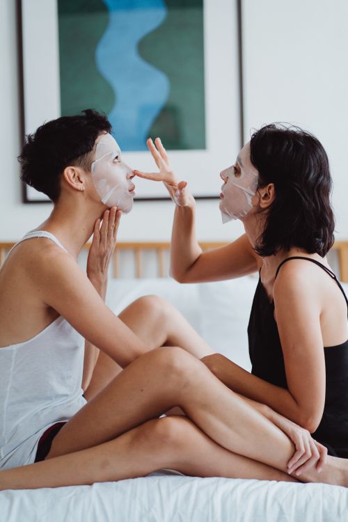 Free Two women enjoying self-care with face masks in a cozy bedroom environment. Stock Photo