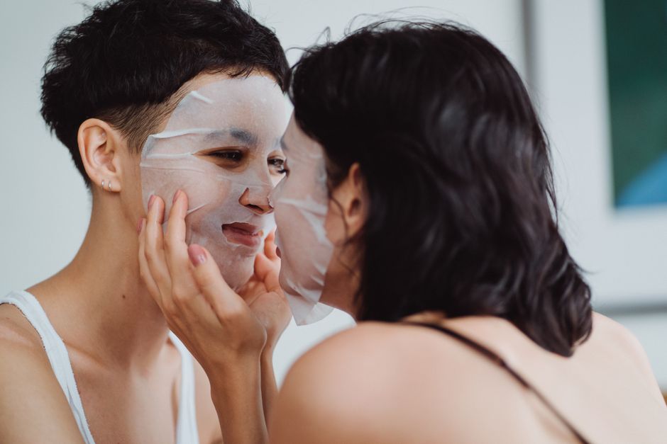 Two women enjoying a bonding moment with facial sheet masks, smiling intimately.