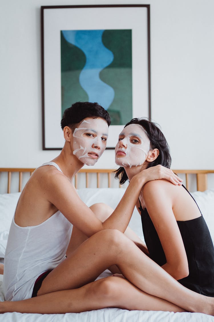 A Couple With Sheet Mask Sitting On The Bed