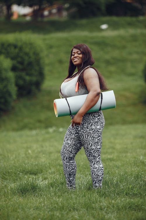 Free Confident woman carrying yoga mat in a green park, ready for outdoor exercise. Stock Photo