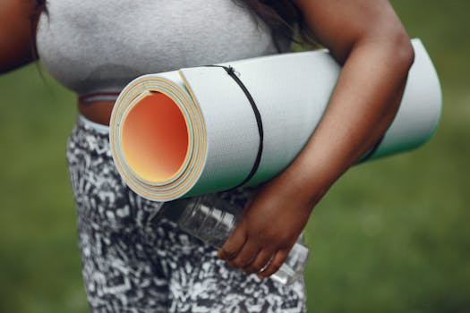 Close-up of a woman holding a yoga mat and water bottle in a park, ready for a workout.