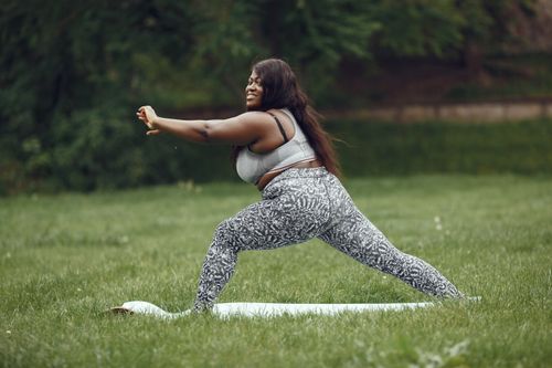 Free A joyful woman practicing yoga outdoors on a mat in a lush park setting. Stock Photo