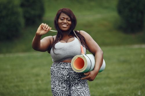 Free Smiling woman outdoors with yoga mat, ready for fitness session in a sunny park. Stock Photo