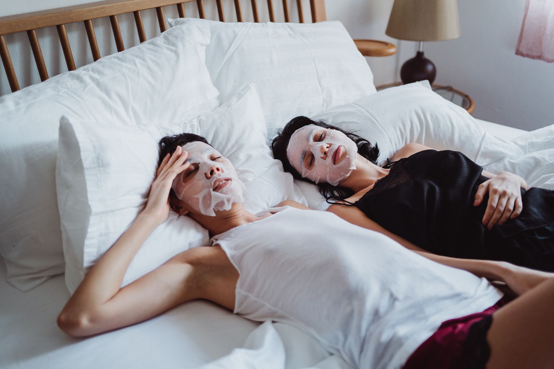 Two adults relaxing in bed with facial masks, enjoying a calm skincare routine.