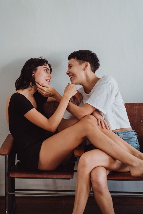 Free Two women seated on wooden chairs, sharing a joyful and intimate moment indoors. Stock Photo