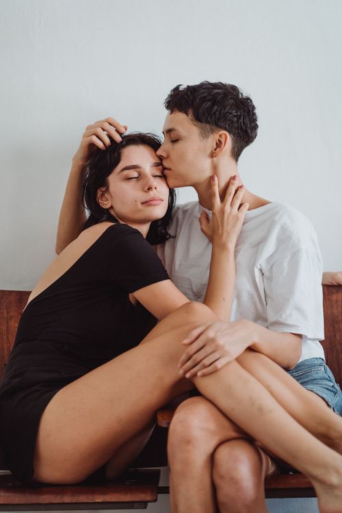 Free Two women embracing with affection, sitting on a wooden bench indoors. Stock Photo