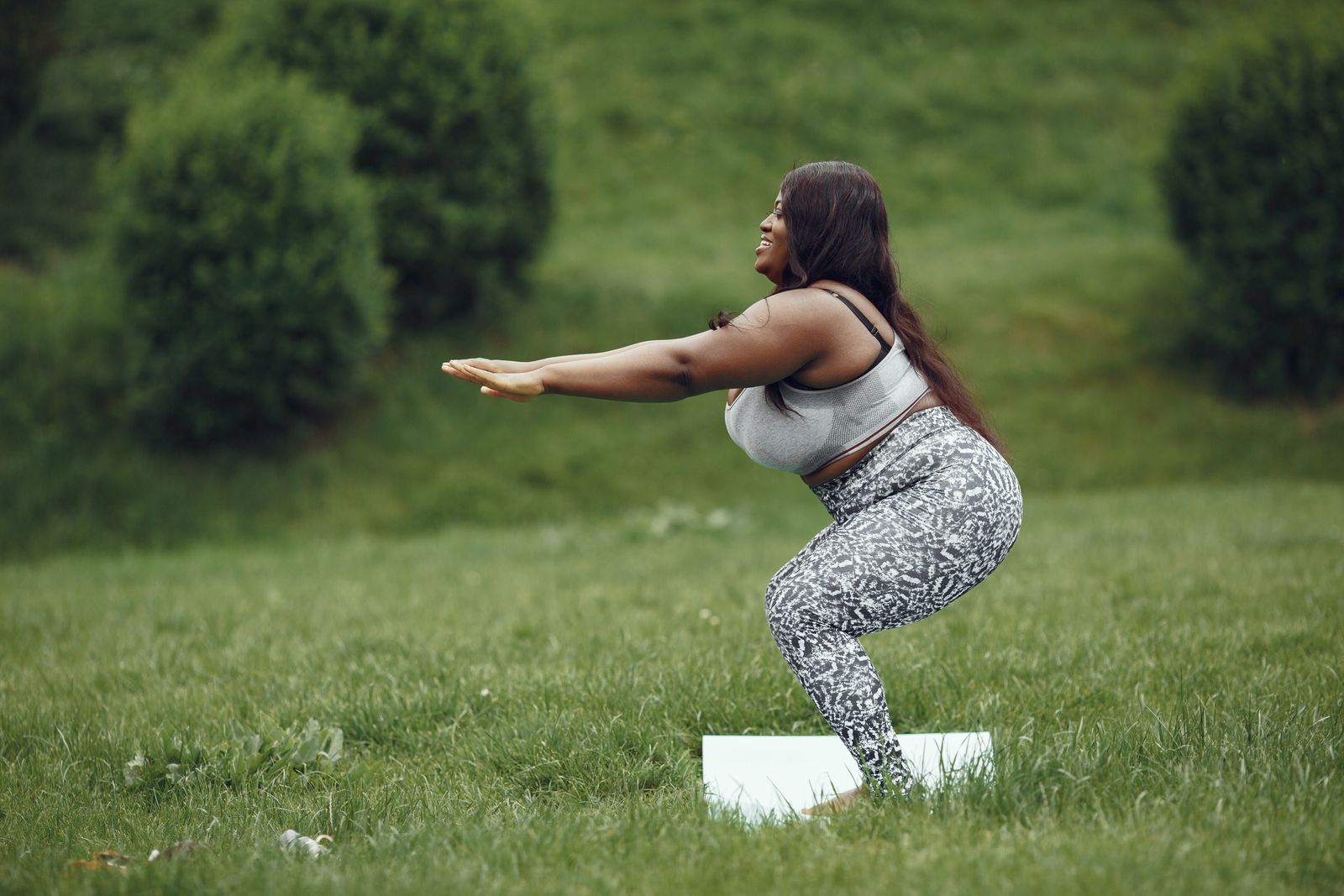 Woman practicing a deep yoga squat similar to Malasana outdoors on grass
