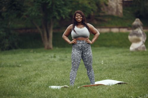 Free A confident plus-size woman standing on grass in activewear with a yoga mat. Stock Photo