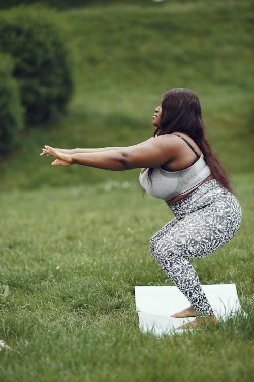 Woman in Gray Top and Leggings Squatting on a Mat on Green Grass