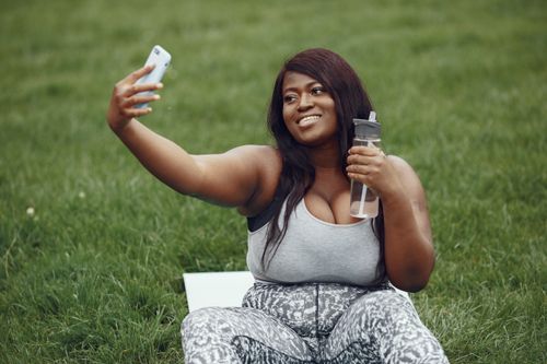 Free A woman sitting on grass, taking a selfie while holding a water bottle. Perfect for lifestyle and fitness themes. Stock Photo