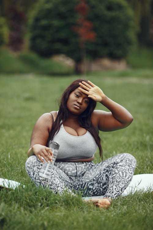 A Woman Holding a Tumbler and Sitting on a Yoga Mat 