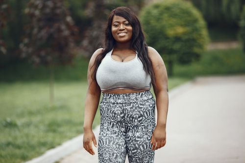 Free Smiling plus-size woman in activewear, enjoying an outdoor walk on a sunny day. Stock Photo