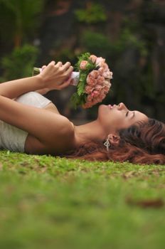 A serene image of a woman lying down outdoors, holding a bouquet of flowers.
