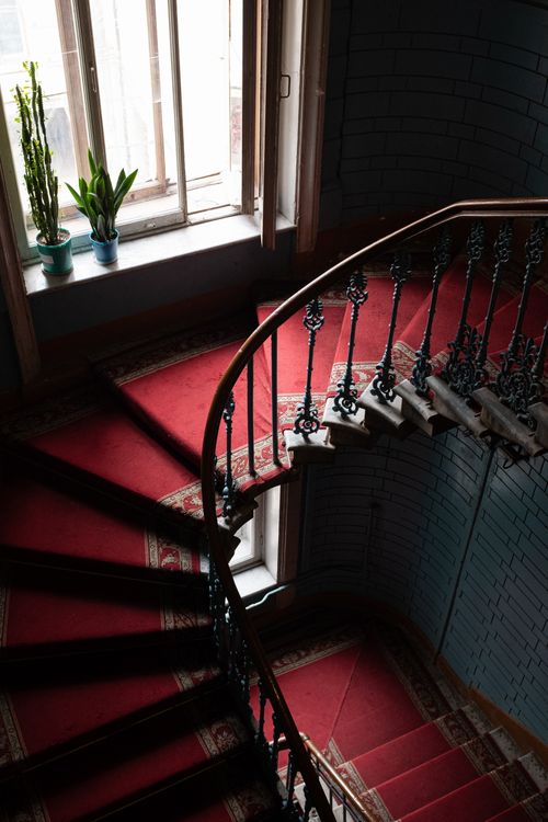 Free A beautifully detailed vintage spiral staircase with ornate wrought iron railing, red carpet, and natural light. Stock Photo