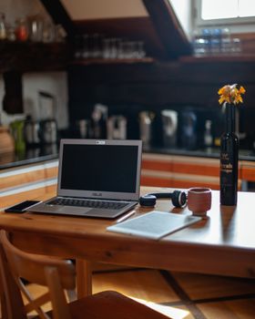 A cozy rustic kitchen table setup with laptop and accessories in natural lighting.
