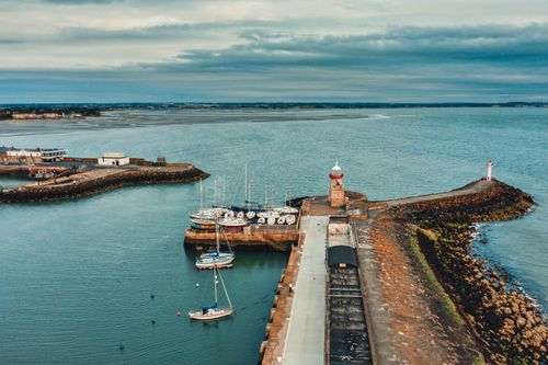 Free Scenic aerial shot of Dublin's coastline featuring a prominent lighthouse and docking boats. Stock Photo