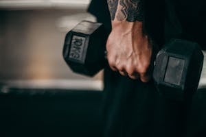 Person Holding Black Dumbbell With Black Tattoo