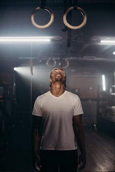 A muscular man in a gym, focusing on gymnastic rings with determination for his workout session.